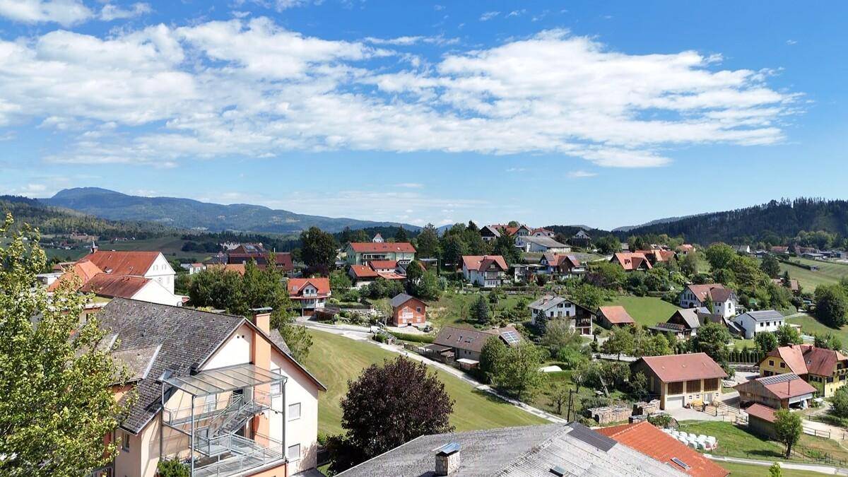 Panoramablick über eine ländliche Siedlung mit vielen Häusern und grünen Hügeln im Hintergrund.