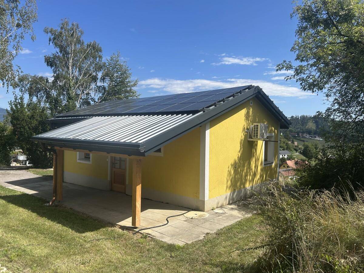 Seitenansicht eines gelben Hauses mit Solaranlage, Klimaanlage und überdachtem Eingang.