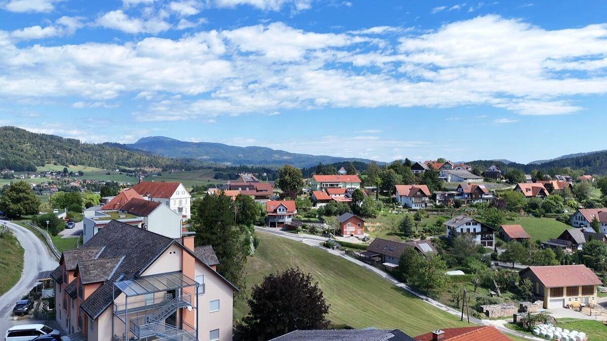 Weitläufiger Blick über eine ländliche Siedlung mit Häusern und grünen Hügeln.