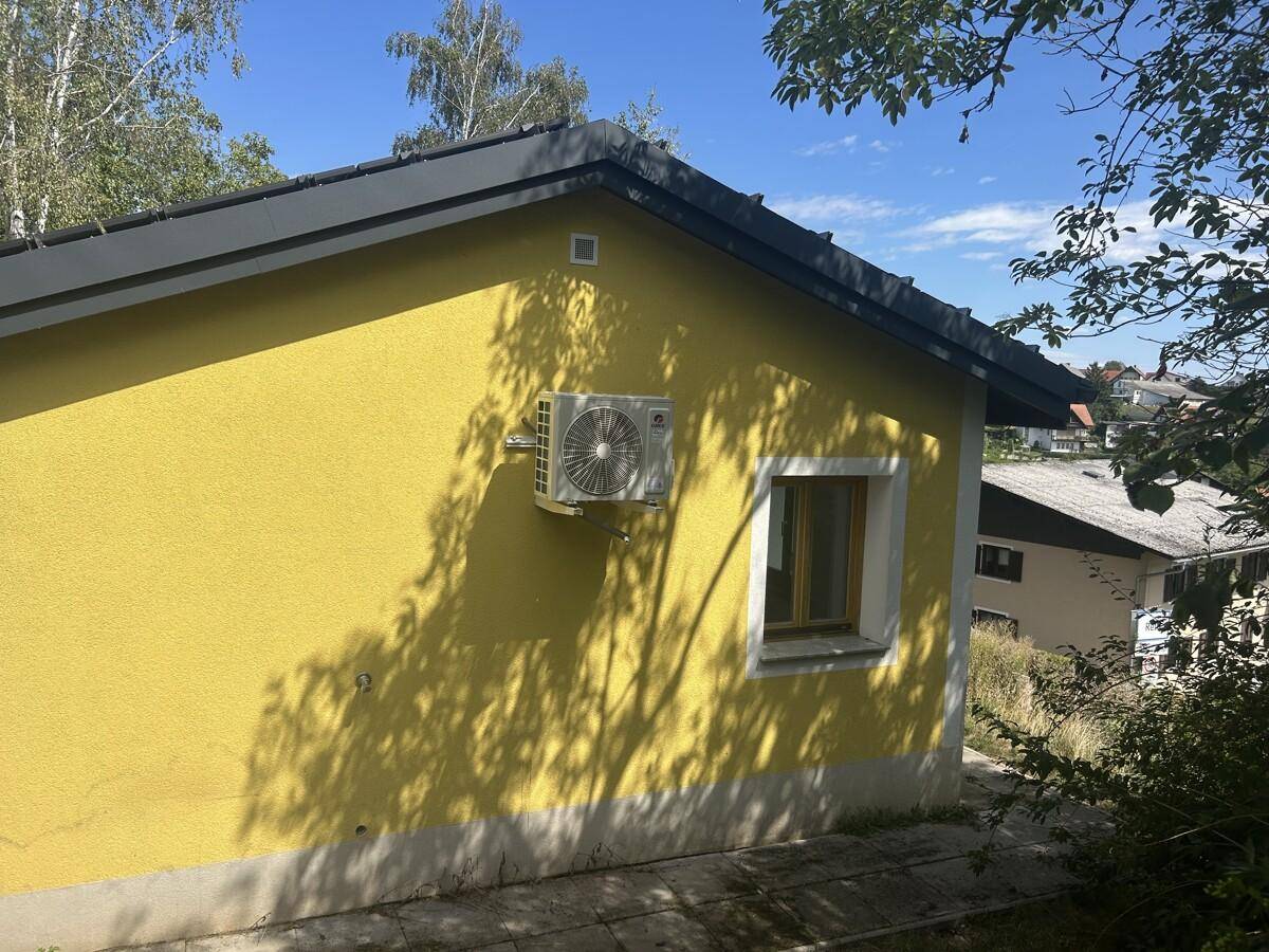 Seitenansicht eines gelben Hauses mit Klimaanlage an der Fassade und Schattenwurf.