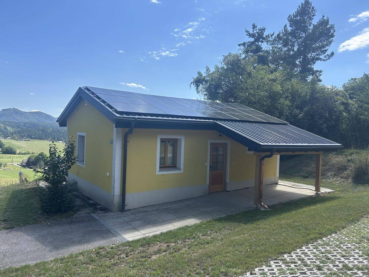 Seitenansicht eines gelben Hauses mit Solaranlage und überdachtem Eingangsbereich.
