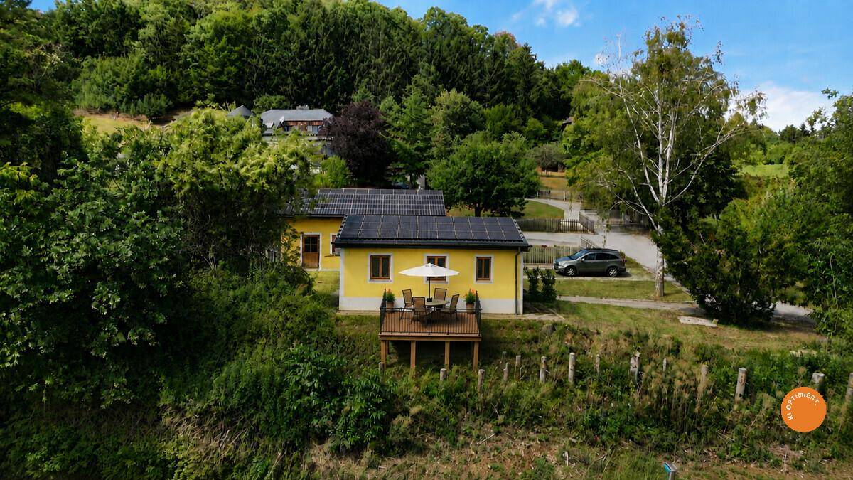 Vogelperspektive eines gelben Hauses mit möblierter Holzterrasse und Solaranlage.
