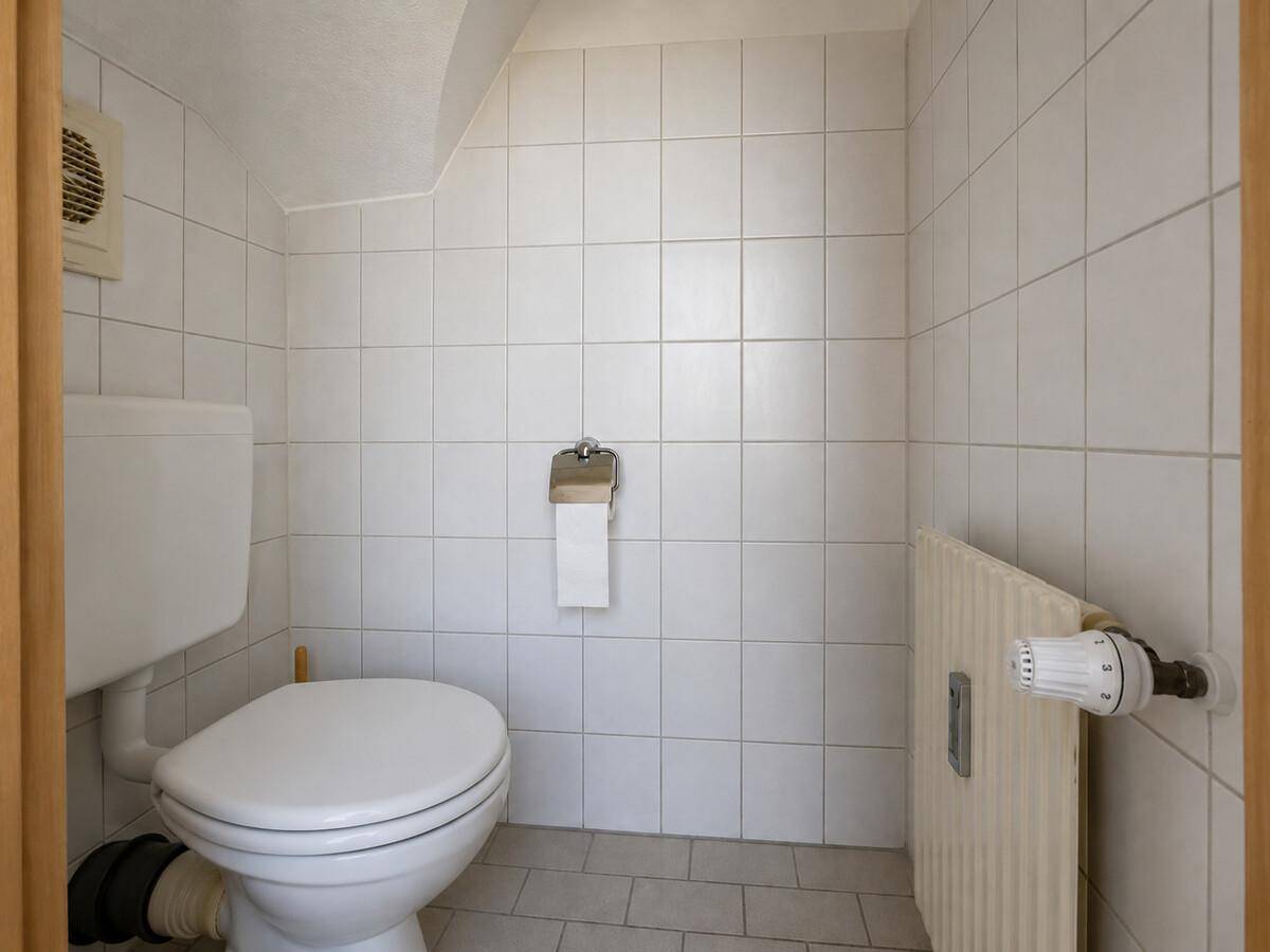 Kleines Gäste-WC mit weißen Fliesen und Toilette, funktional und sauber.