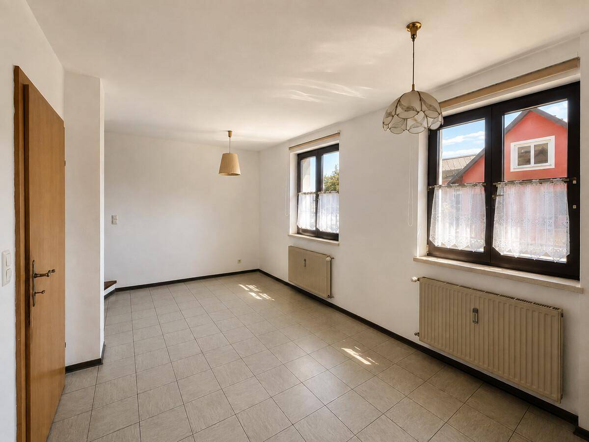 Geräumiger Wohnbereich mit Fliesenboden und großen Fenstern, bietet viel Tageslicht.