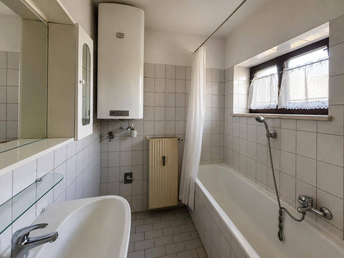 Funktionales Badezimmer mit Badewanne, Waschbecken und Fenster, hell gefliest.