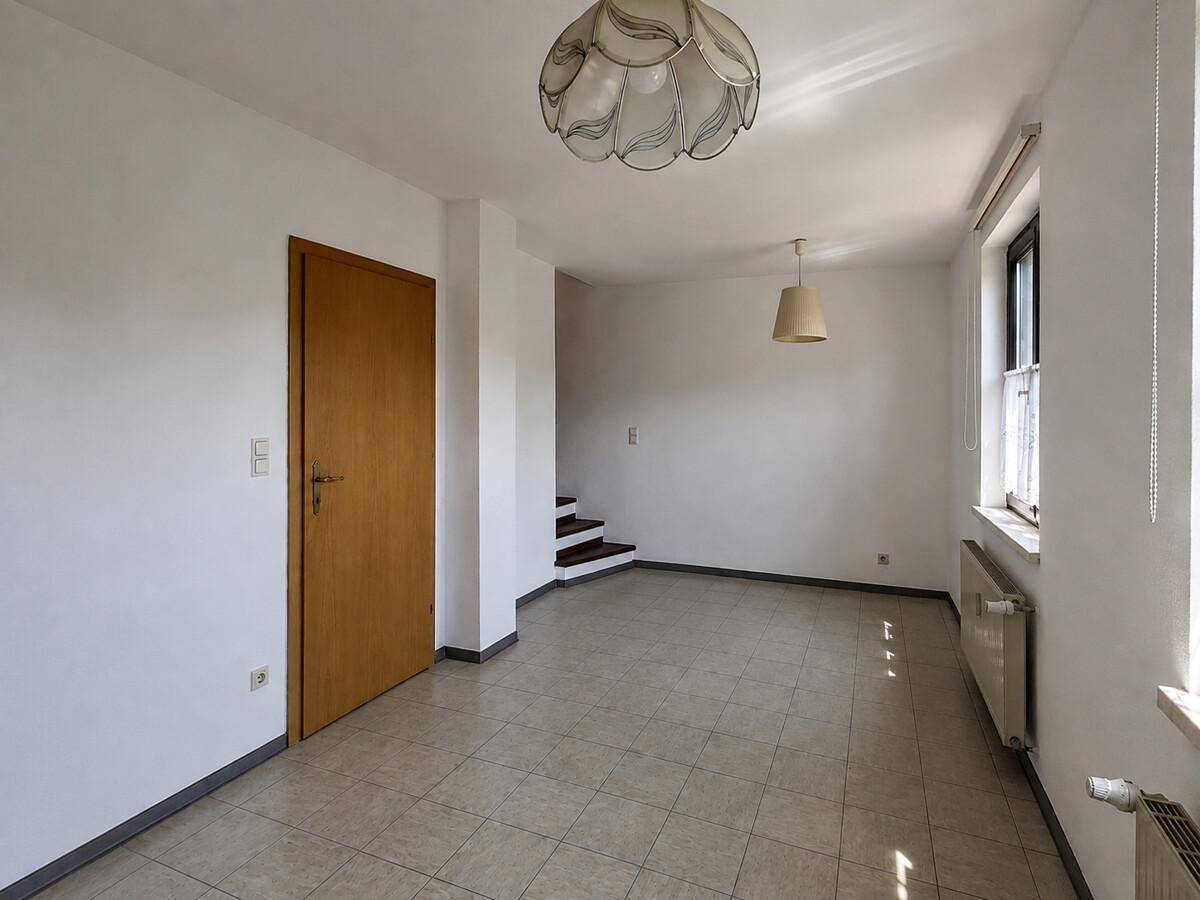Heller Wohnbereich mit Fliesenboden und Zugang zu einer Treppe, bietet vielseitige Nutzungsmöglichkeiten.