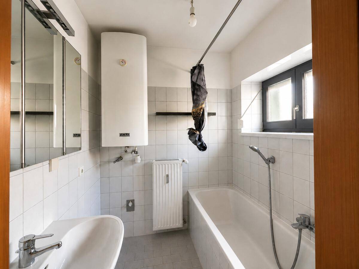 Funktionales Badezimmer mit Badewanne, Waschbecken und Fenster, hell gefliest.