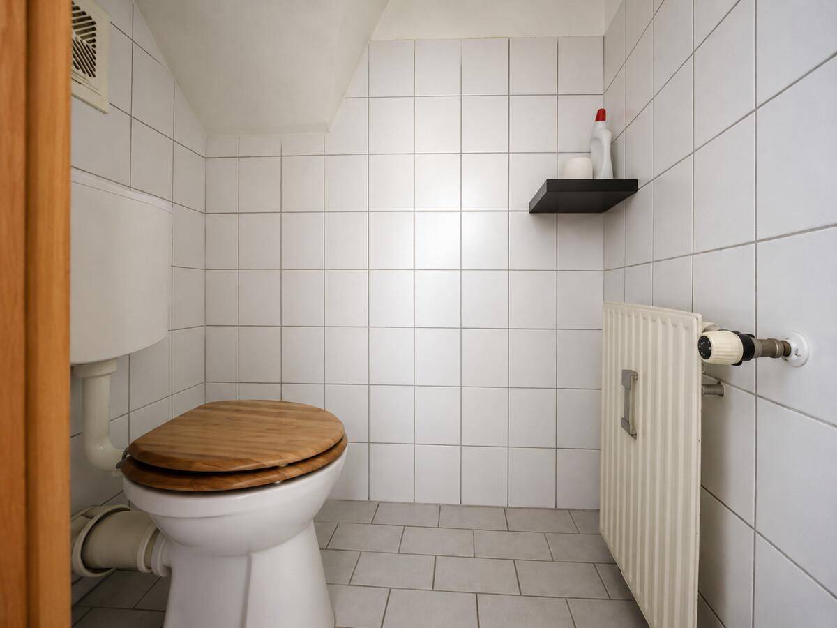 Kleines Gäste-WC mit weißen Fliesen und Holz-Toilettensitz, funktional und sauber.