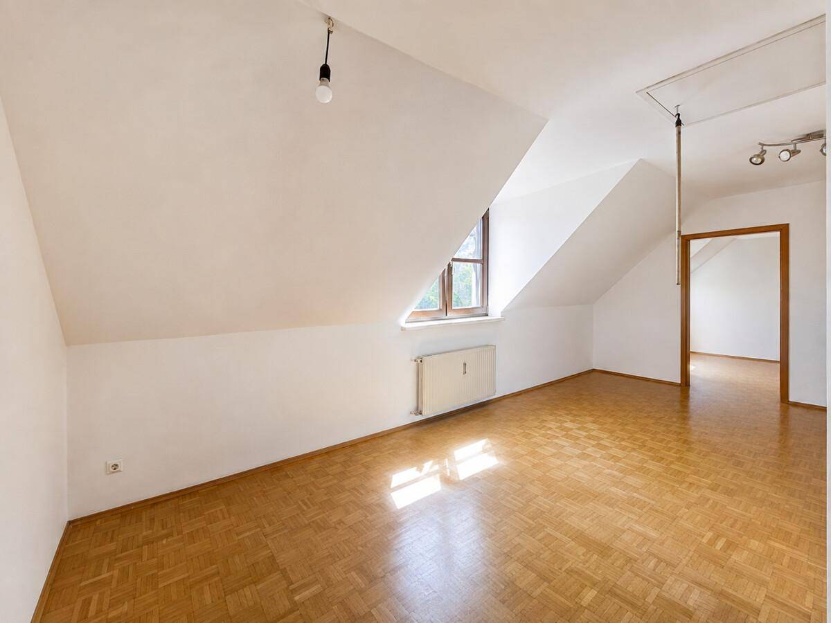 Geräumiger Dachbodenraum mit schrägen Decken, Holzparkett und einem Fenster für Tageslicht.