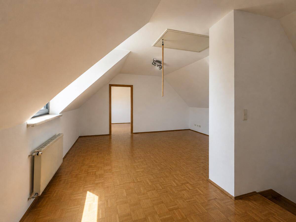 Heller Dachbodenraum mit schrägen Wänden, Parkettboden und Zugang zu weiteren Räumen.