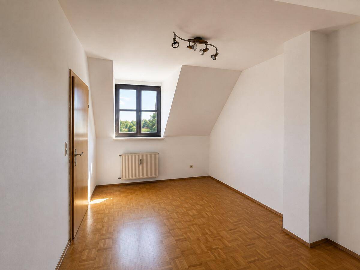 Helles Zimmer mit Parkettboden, schräger Decke und Blick ins Grüne durch das Fenster.