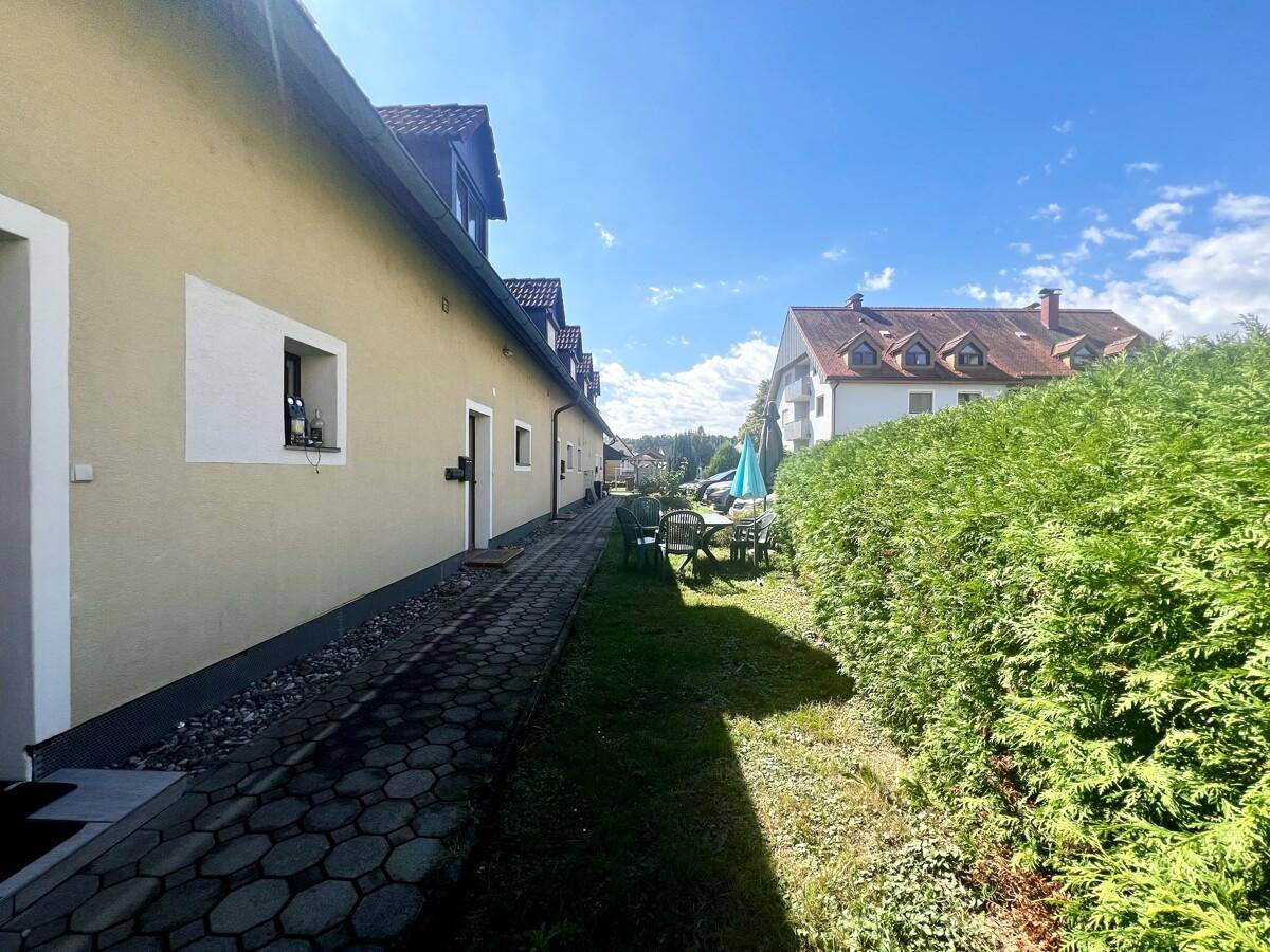 Reihenhäuser mit gepflastertem Weg, grüner Hecke und Sitzgelegenheiten im Außenbereich.