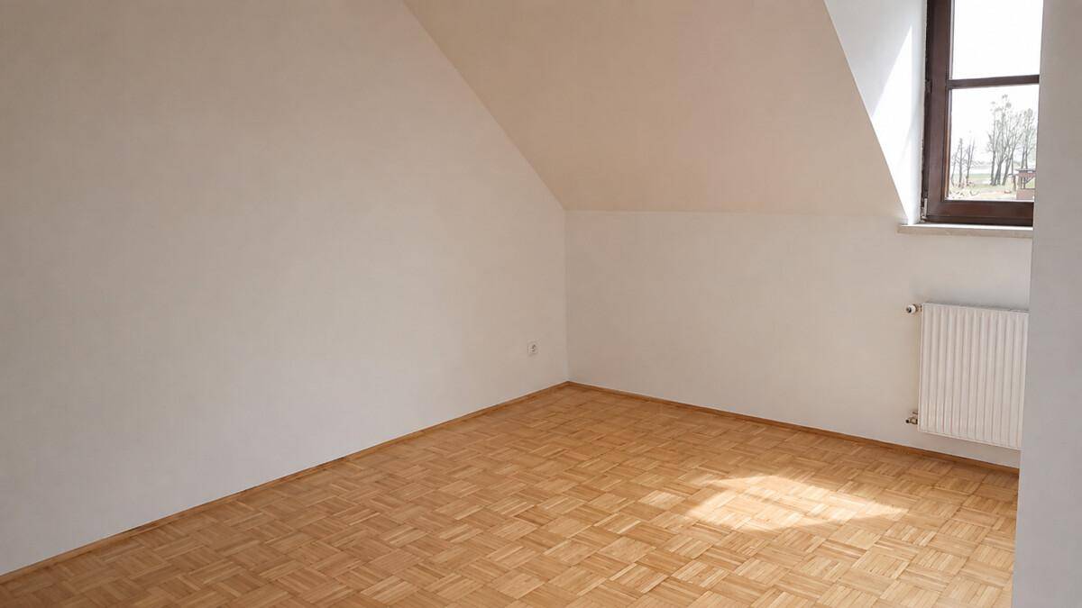 Geräumiger Dachbodenraum mit schrägen Decken, Holzparkett und einem Fenster für Tageslicht.