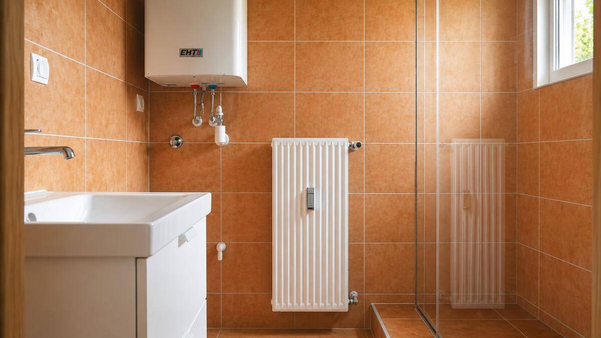 Badezimmer mit orangefarbenen Fliesen, Duschkabine, Waschbecken und Fenster für Tageslicht.