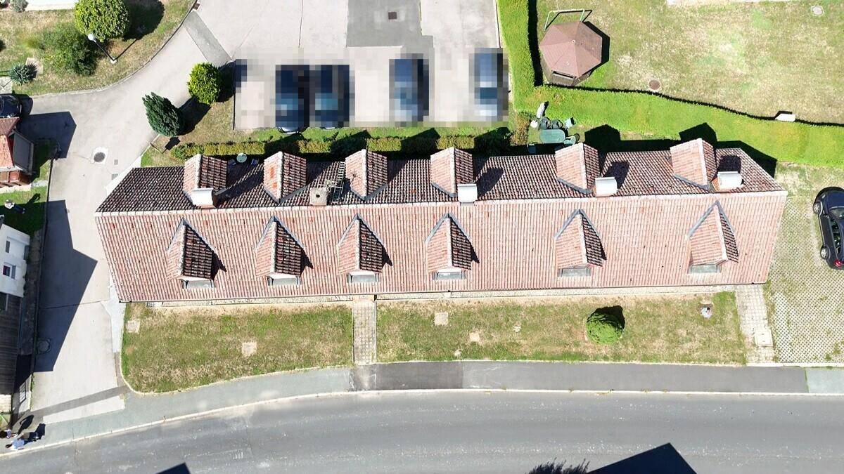 Draufsicht auf das Ziegeldach des Gebäudes mit Gauben, Parkplätzen und einem grünen Gartenbereich.