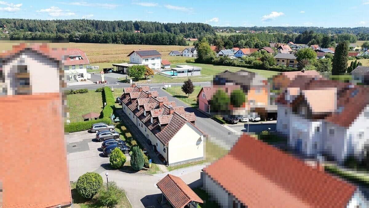 Weitläufige Luftaufnahme des Gebäudes in einer ländlichen Wohnsiedlung mit Feldern und Wäldern im Hintergrund.