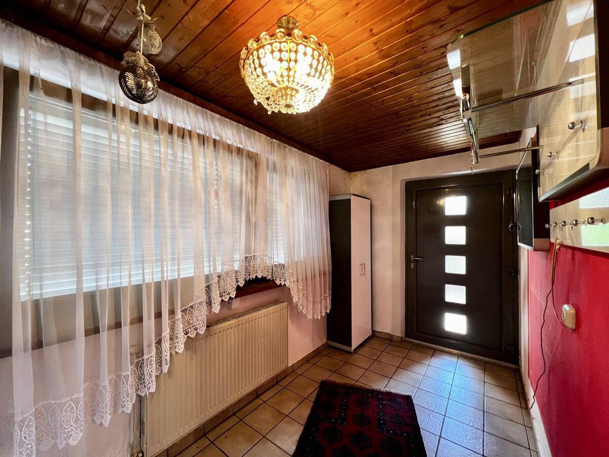 Eingangsbereich mit rustikaler Holzdecke, Fliesenboden und einem Fenster mit Vorhängen.