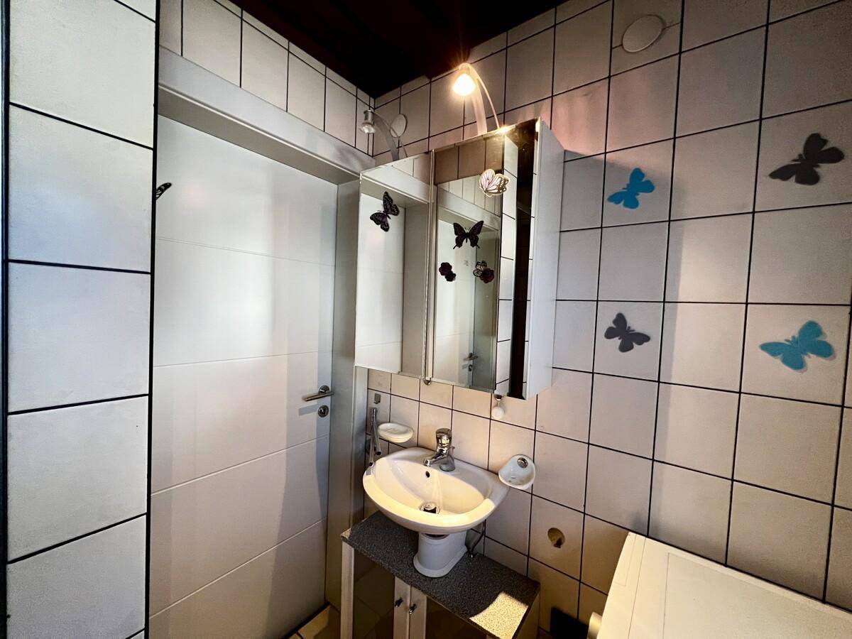 Kleines Badezimmer mit Waschbecken, Spiegelschrank und weißen Fliesen, dekoriert mit Schmetterlingen.