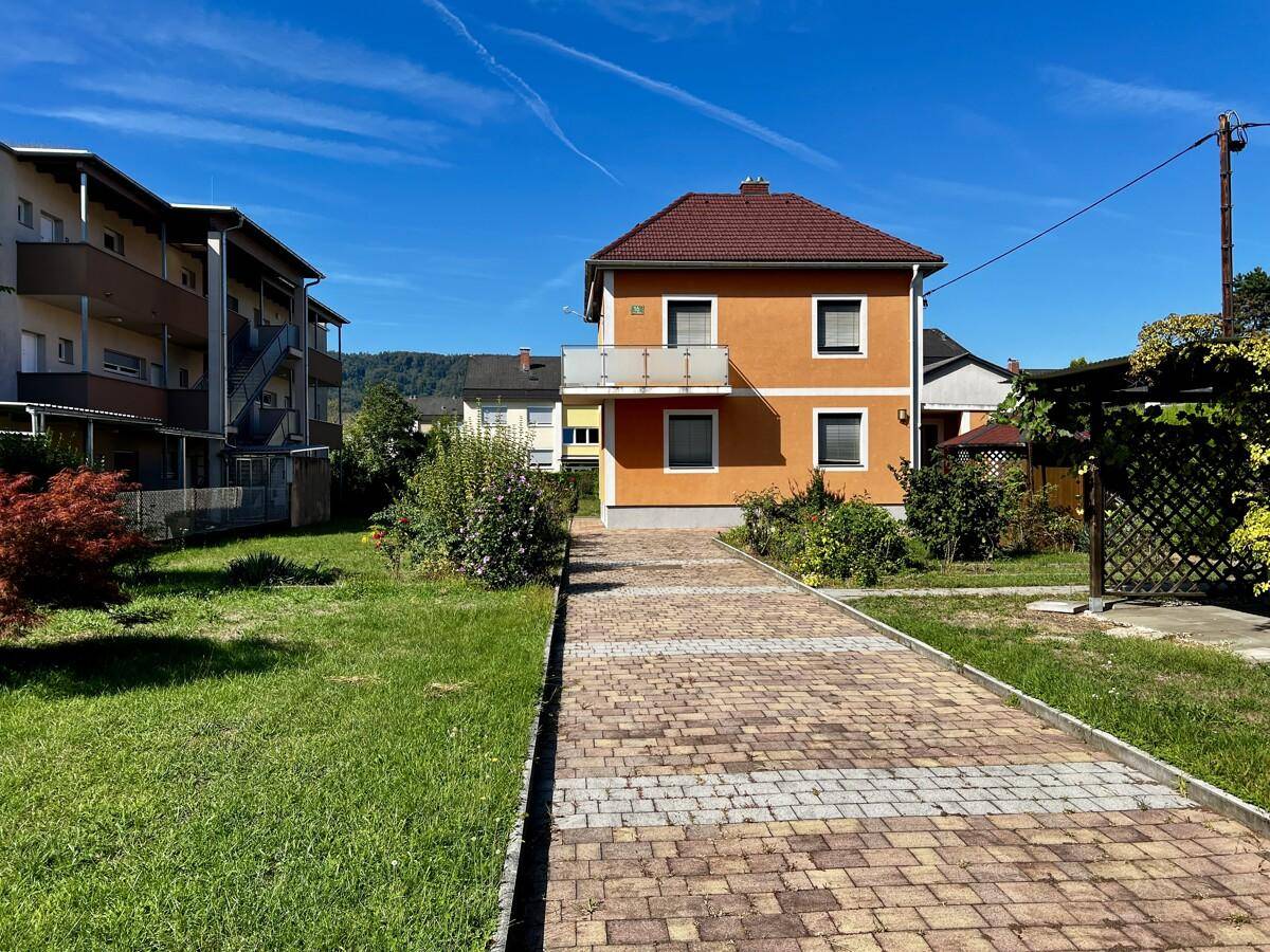 Vorderansicht des orangefarbenen Hauses mit Balkon, gepflasterter Auffahrt und grünem Vorgarten.