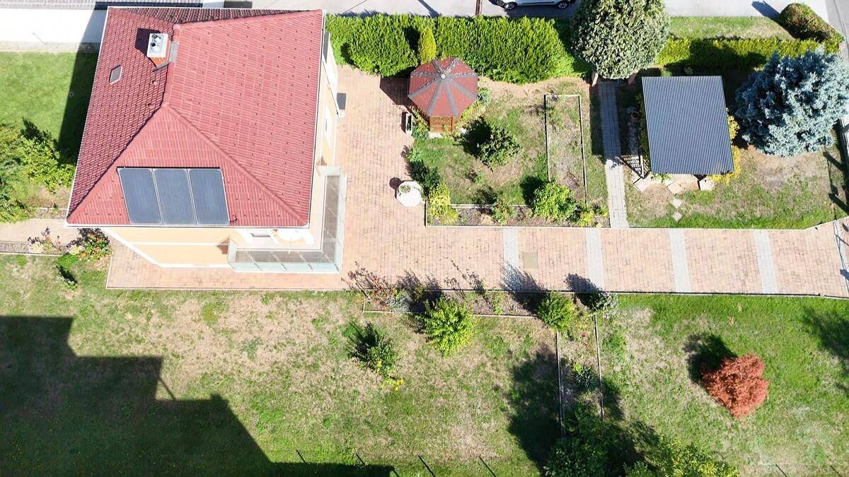 Vogelperspektive des Hauses mit rotem Dach, Solaranlage und gepflastertem Gartenweg.