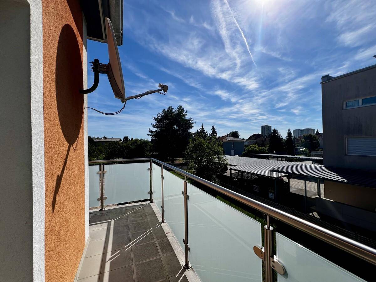 Balkon mit moderner Glasbrüstung und Blick auf die Umgebung unter blauem Himmel.