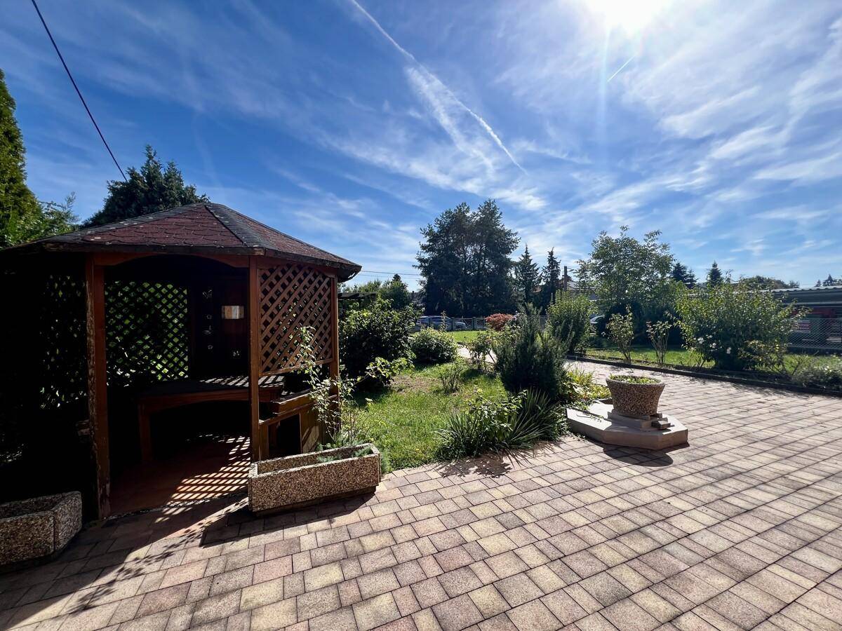 Gepflasterter Gartenbereich mit einem charmanten Holzpavillon und Pflanzen in voller Sonne.