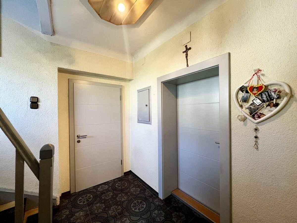 Heller Flur mit Aufzugstür, Treppenaufgang und dekorativen Elementen an der Wand.