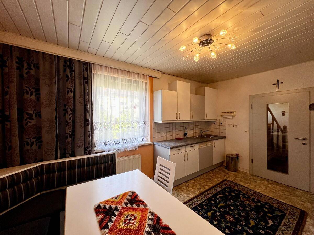 Helle Wohnküche mit Essbereich, Fenster und Zugang zum Flur, ausgestattet mit weißen Schränken.