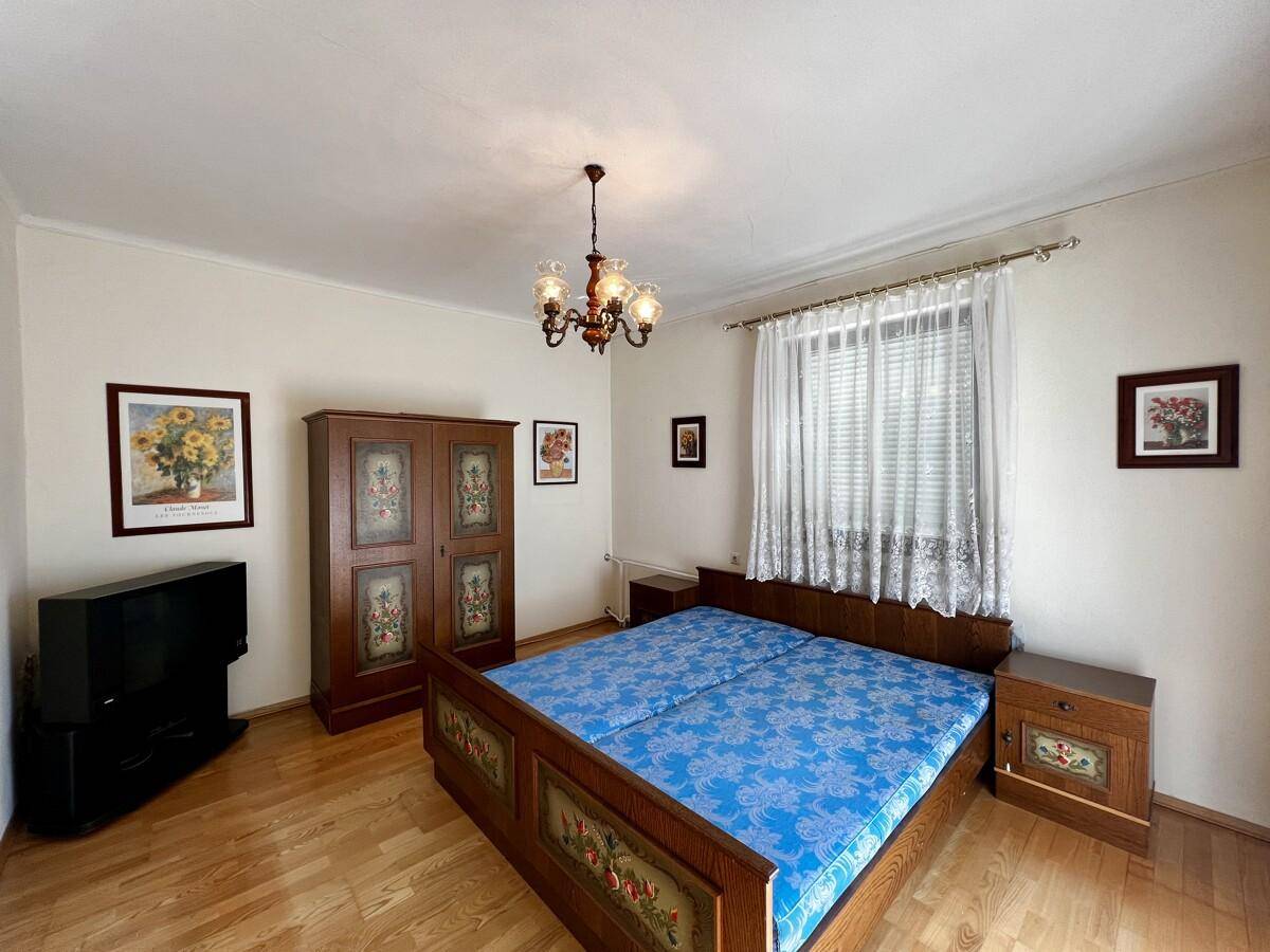 Schlafzimmer mit Doppelbett, traditionellem Holzschrank und Parkettboden, gut beleuchtet.