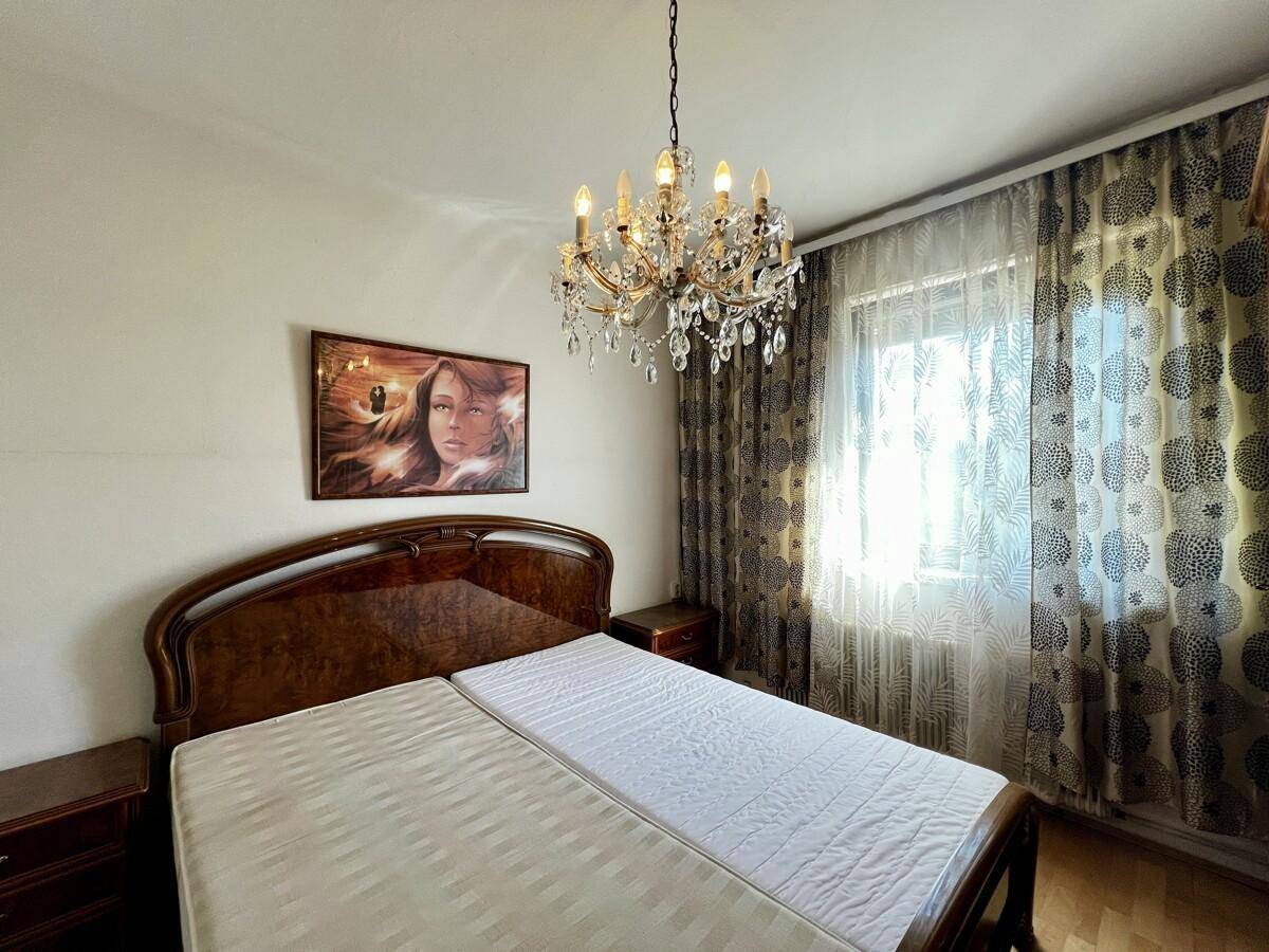Schlafzimmer mit Doppelbett, elegantem Kristallleuchter und Vorhängen am Fenster.