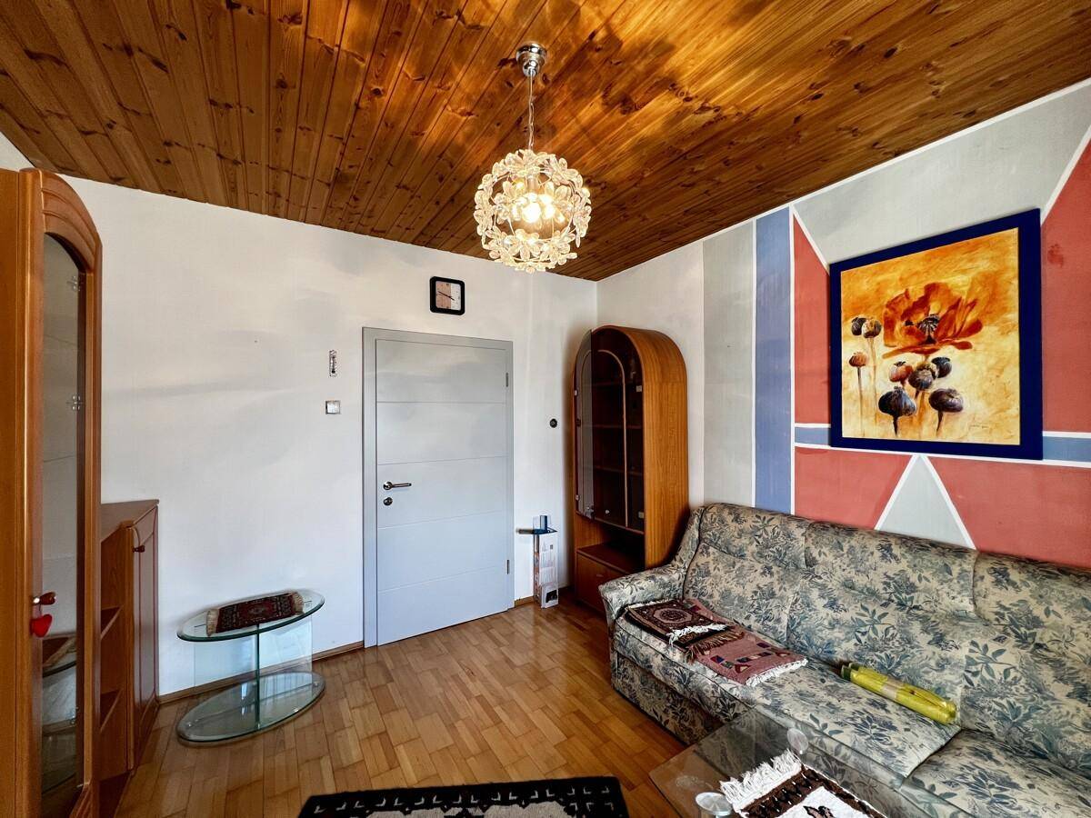 Gemütliches Wohnzimmer mit Sofa, Holzdecke und Parkettboden, dekoriert mit einem modernen Bild.