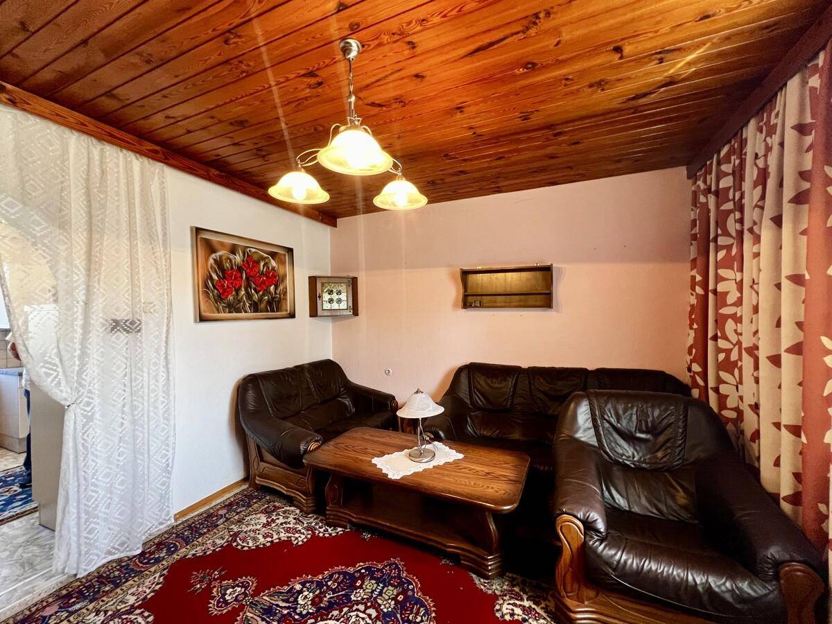 Traditionelles Wohnzimmer mit dunklen Ledersofas, Holztisch und einer rustikalen Holzdecke.