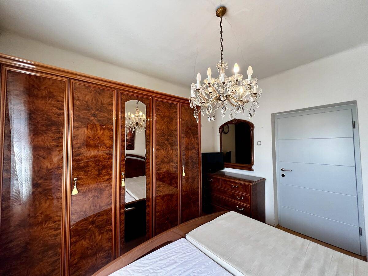Schlafzimmer mit großem Holzschrank, Kristallleuchter und Parkettboden, hell und geräumig.