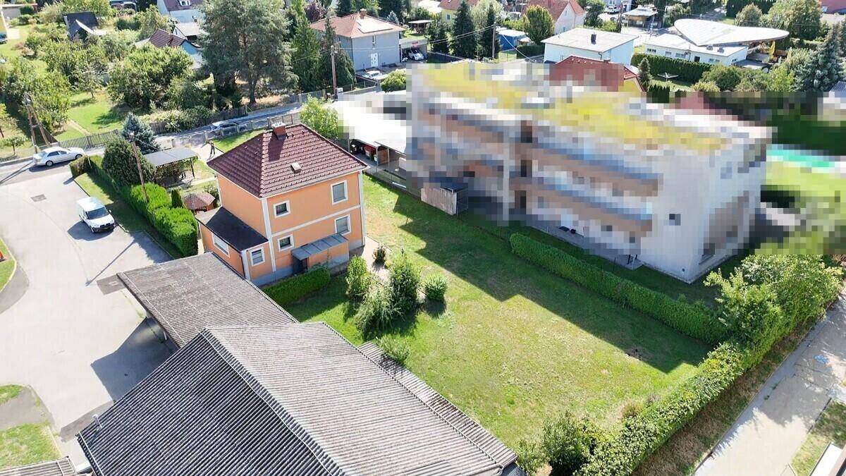 Luftaufnahme des Hauses mit Garten, Carport und angrenzenden Gebäuden in der Nachbarschaft.