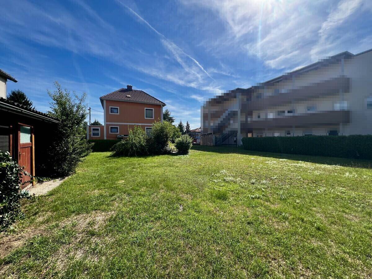 Großer, gepflegter Garten mit Rasenfläche und Blick auf das orangefarbene Einfamilienhaus.