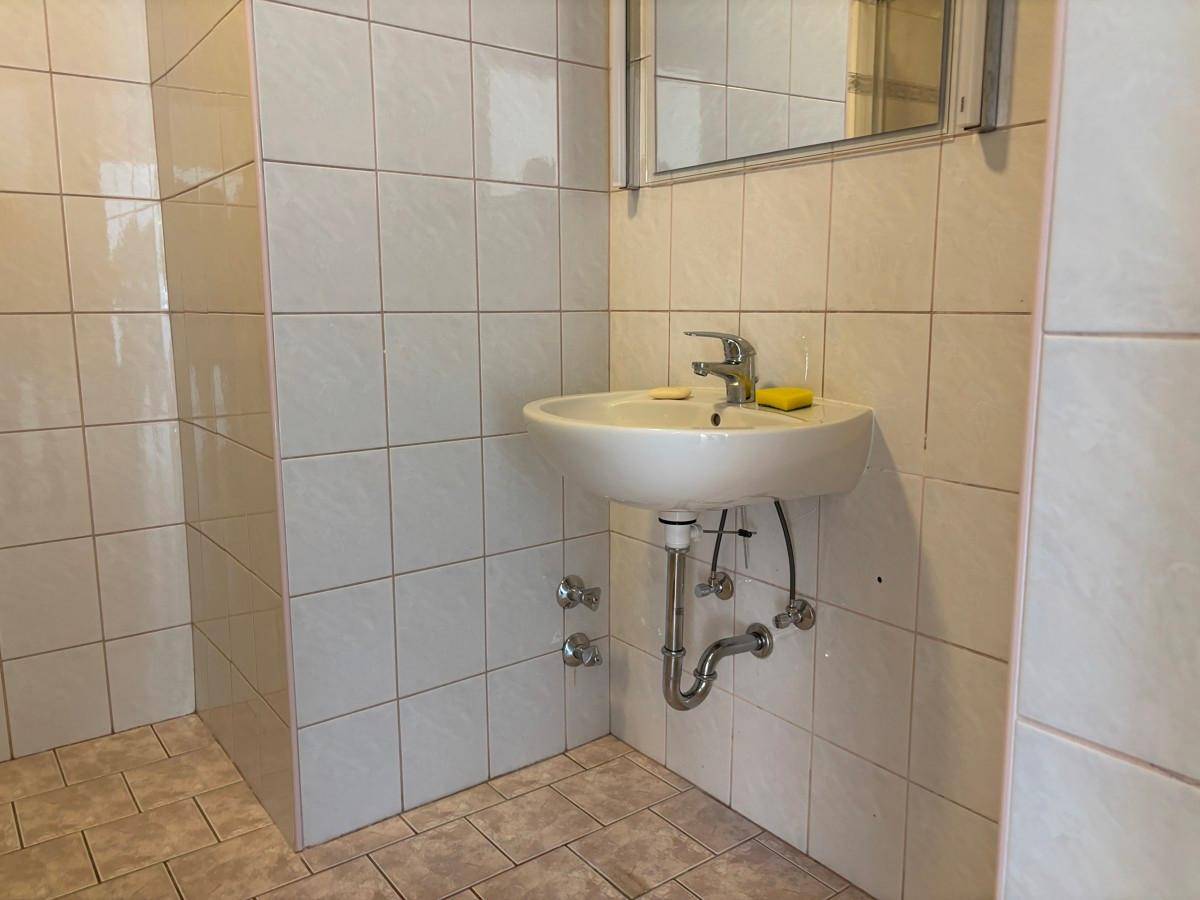 Badezimmer mit weißen Fliesen, einem einzelnen Waschbecken und einem Spiegelschrank.
