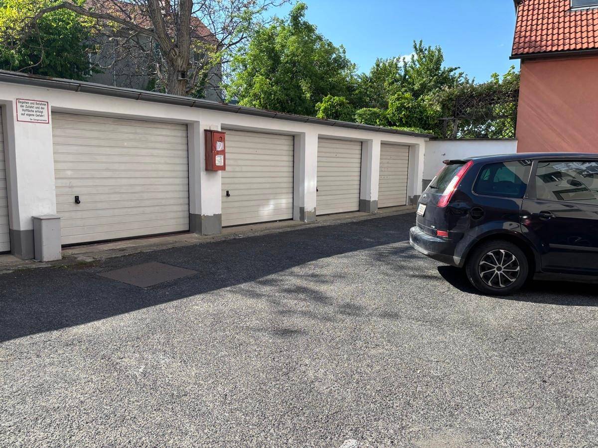 Reihe von Garagen mit Rolltoren und einem geparkten Auto auf dem asphaltierten Hof.