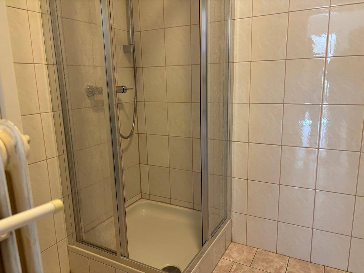 Badezimmer mit weißen Fliesen und einer Duschkabine, die eine praktische Raumnutzung bietet.