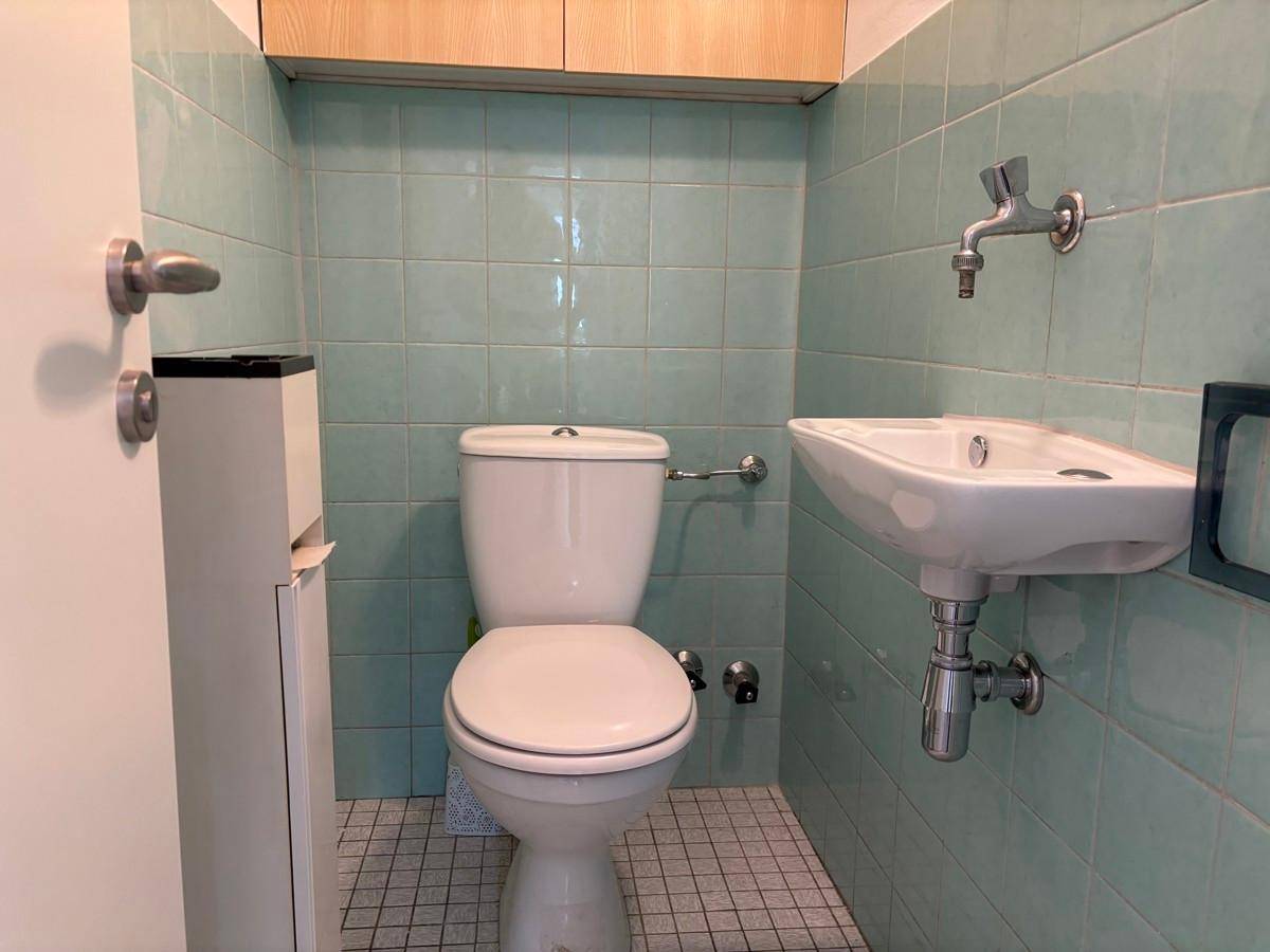 Separate Toilette mit hellblauen Fliesen, WC und einem kleinen Handwaschbecken.