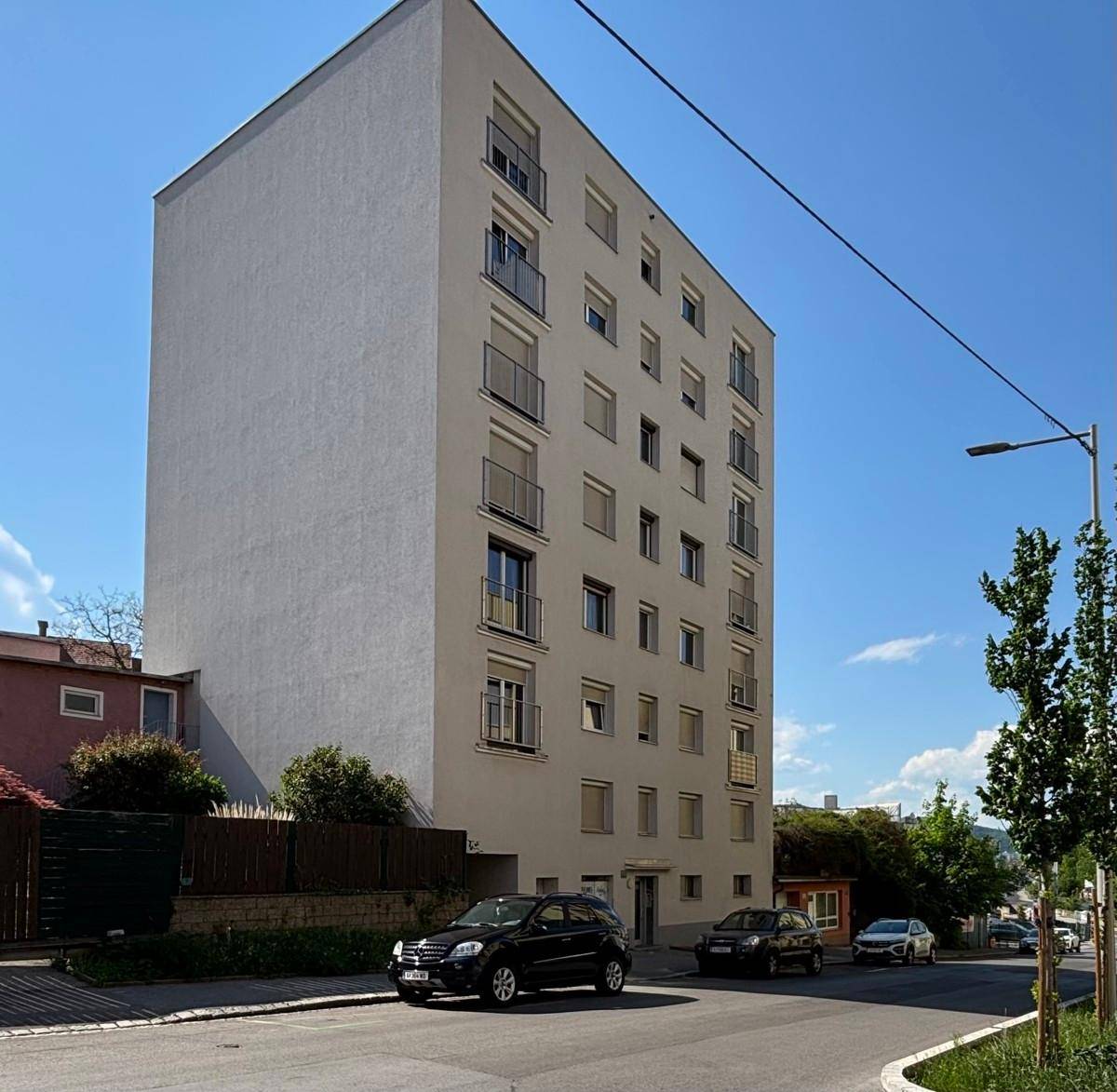 Modernes Mehrfamilienhaus mit schlichter Fassade und Balkonen unter klarem blauem Himmel.