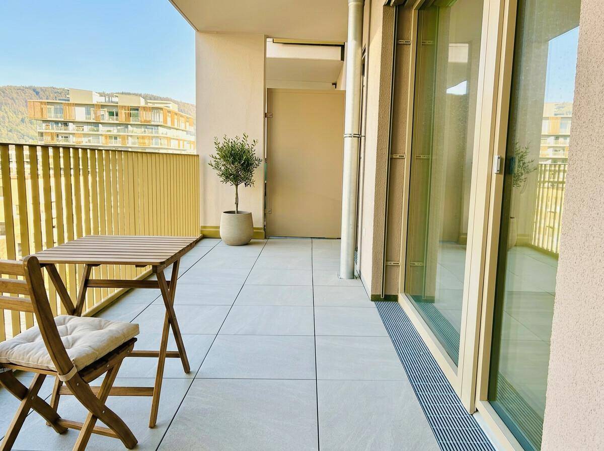 Geräumiger Balkon mit Fliesenboden, Sitzgelegenheiten und Blick auf die umliegenden Gebäude und Hügel.