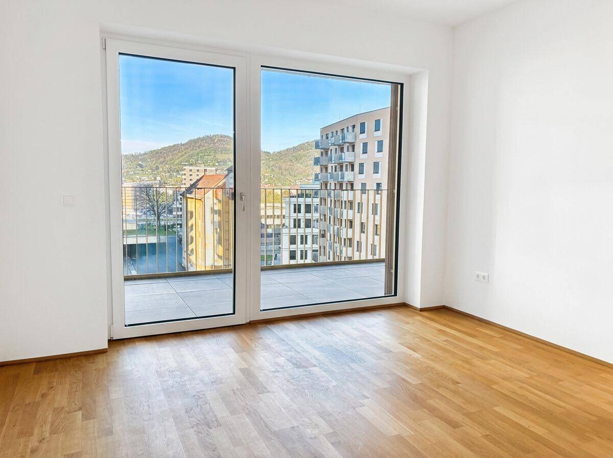 Heller, leerer Raum mit Parkettboden und großen Fenstern, die einen Stadt- und Hügelblick bieten.