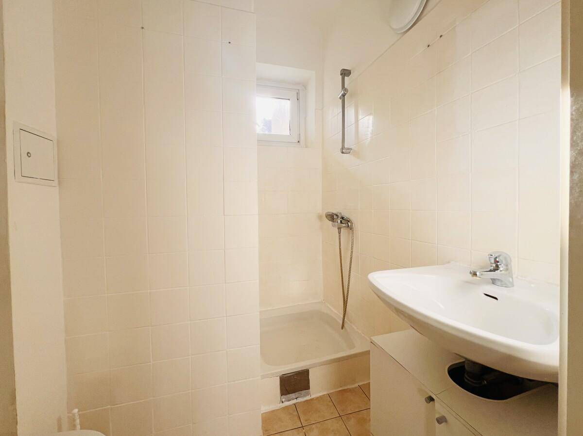 Badezimmer mit Dusche, Waschbecken mit Unterschrank und kleinem Fenster.