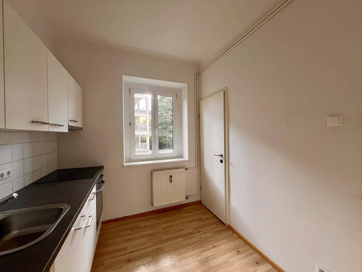 Funktionale Küche mit weißen Oberschränken, Spüle und Blick ins Grüne durch das Fenster.