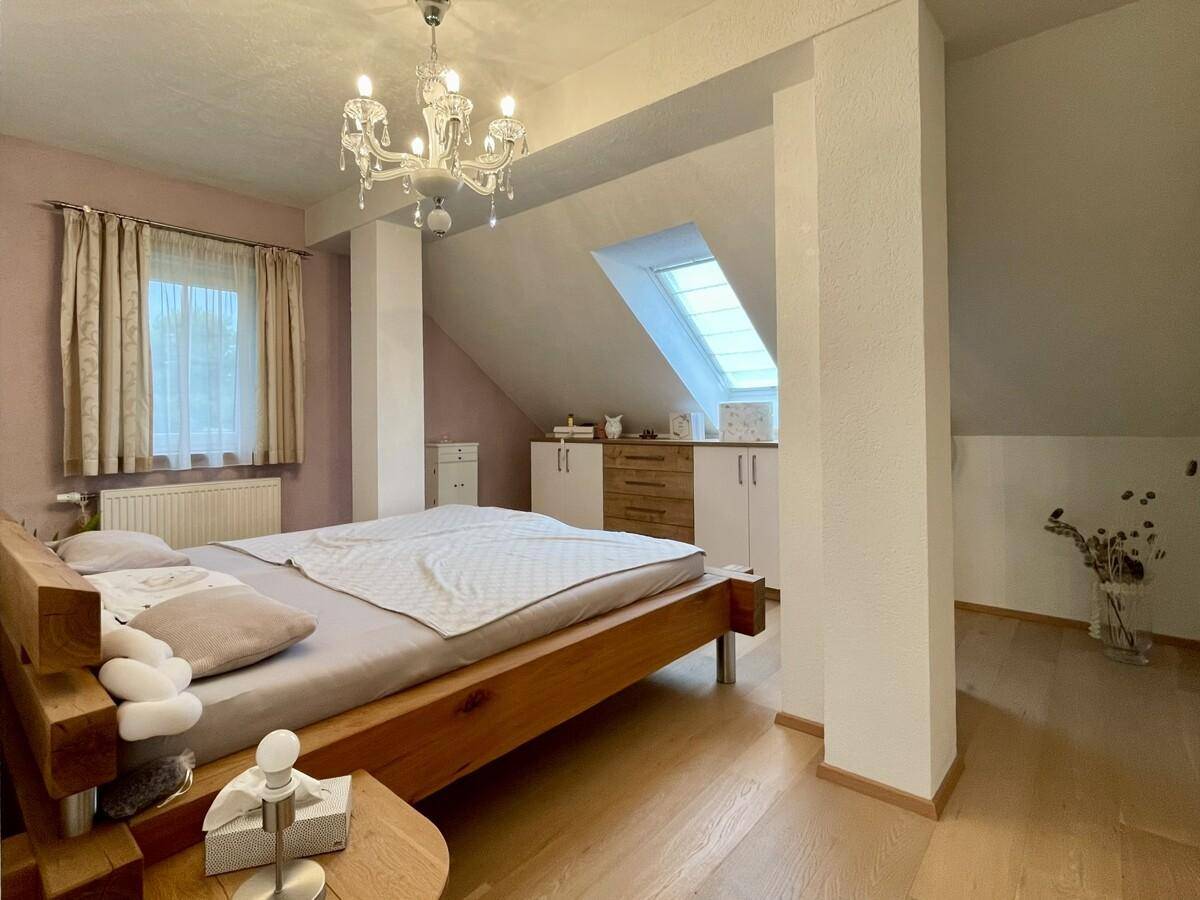 Gemütliches Schlafzimmer im Dachgeschoss mit Holzbett, Dachfenster und Kronleuchter.