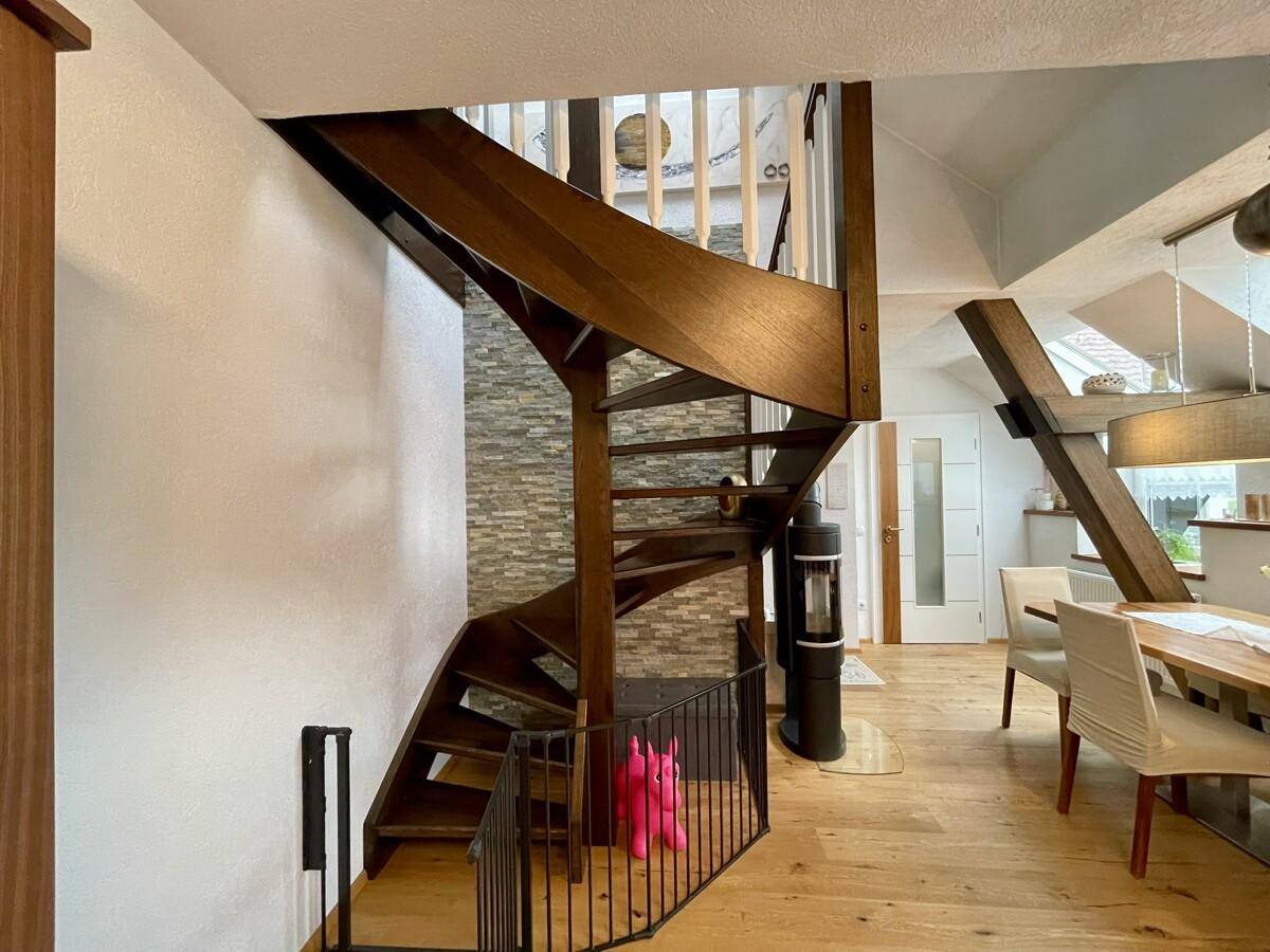 Elegante Holztreppe mit Steinwandakzent und Blick in den offenen Wohnbereich.