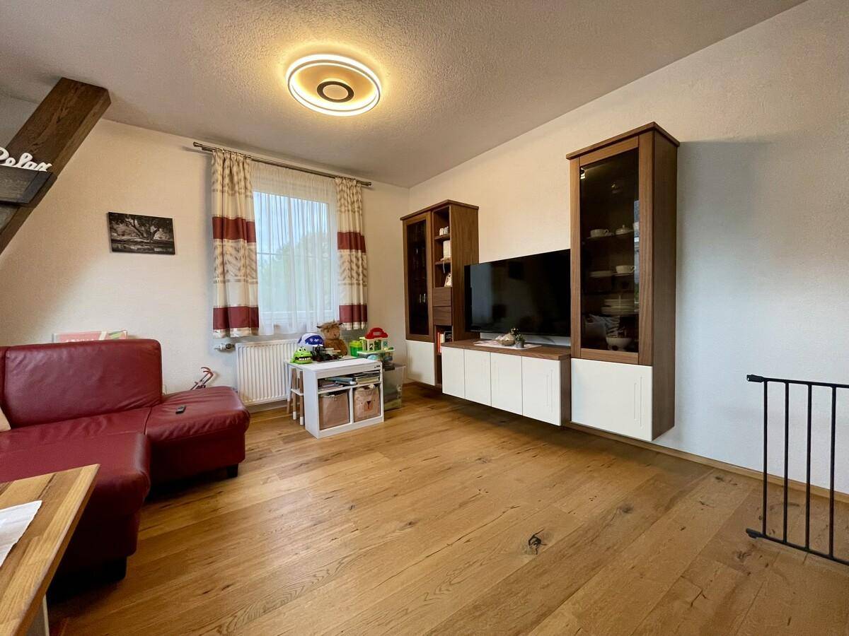 Helles Wohnzimmer mit rotem Sofa, TV-Möbeln und hellem Holzboden.
