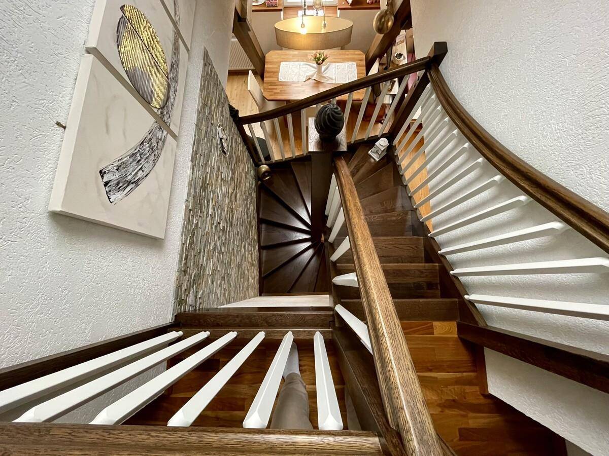 Blick von oben auf eine elegante Holztreppe, die zu einem Essbereich führt.