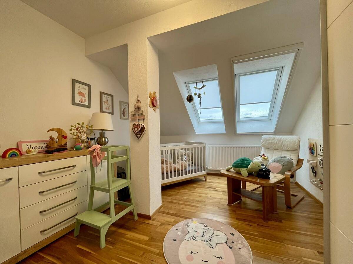 Helles Kinderzimmer mit Babybett, Wickelkommode und viel Tageslicht durch Dachfenster.