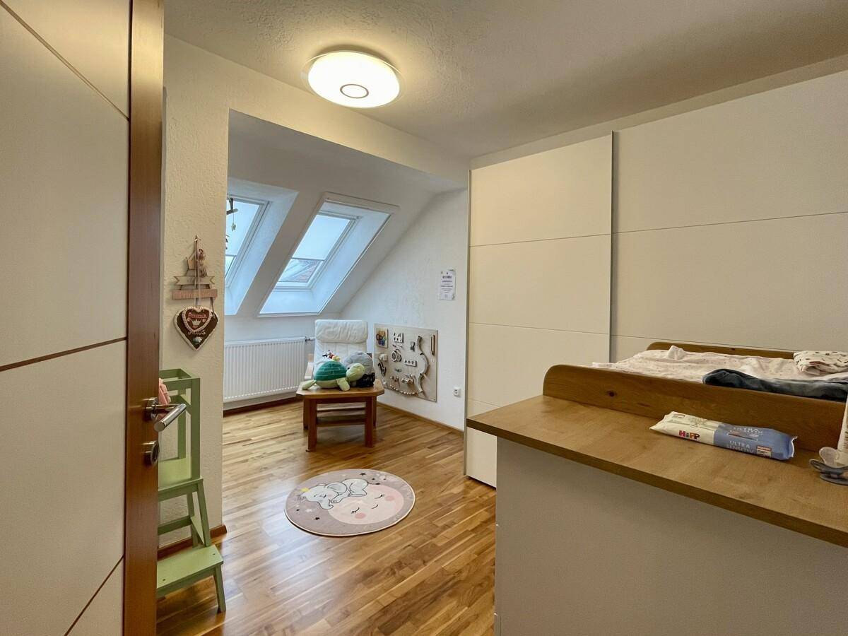 Freundliches Kinderzimmer mit Babybett, Wickeltisch und zwei Dachfenstern.